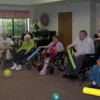 A group of elderly individuals participating in an indoor exercise activity using foam tubes and balls.