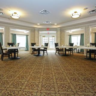 A spacious dining room with several tables and chairs arranged on a patterned carpeted floor.