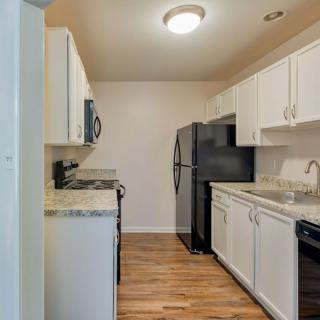 A modern kitchen with white cabinets, black appliances, and a hardwood floor.