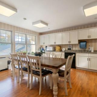 A bright kitchen and dining area with a wooden table and chairs, featuring white cabinets and ample natural light.