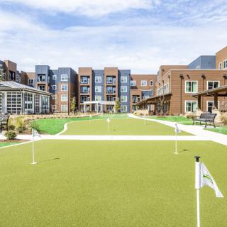 A modern residential building with a well-maintained outdoor lawn and golf putting green under a clear blue sky.