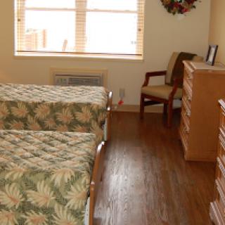 A cozy bedroom featuring two twin beds with floral bedding, a wooden floor, and bright natural light coming from the window.