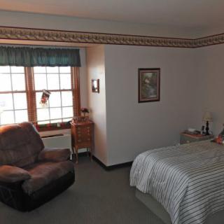 A neatly arranged bedroom with a bed, chair, and window.