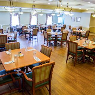 An empty restaurant dining room with neatly arranged tables and chairs on a wooden floor.