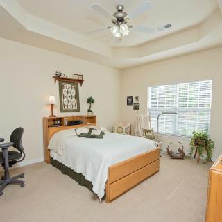 A modern bedroom with a neatly made bed, desk area, and elegant decor, bathed in natural light from a large window.