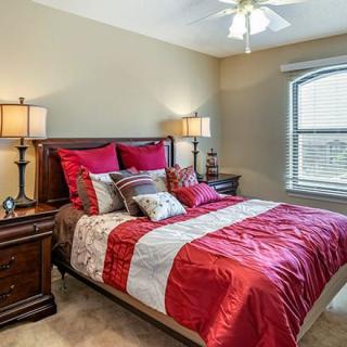A neatly arranged bedroom with red and white bedding and warm lighting.