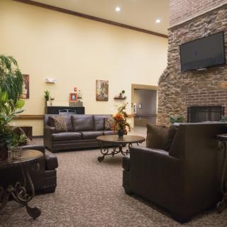 A cozy lobby area with leather sofas, armchairs, a fireplace, and a mounted television.