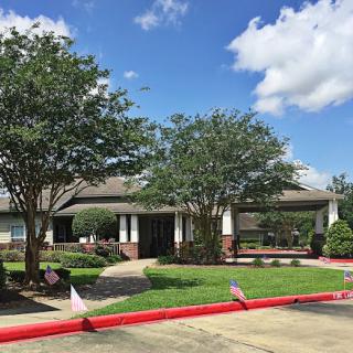 A peaceful view of a well-maintained building surrounded by lush greenery and a clear blue sky.