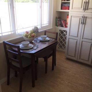 A cozy kitchen nook with a dining table set for two, featuring a fruit bowl and decorative shelves.