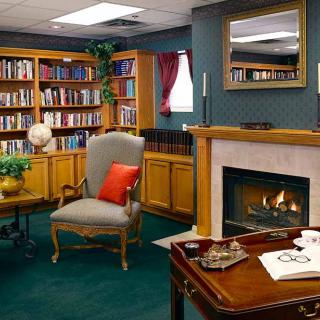 A cozy library room with bookshelves, a fireplace, and comfortable seating.