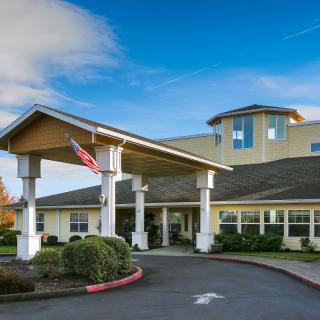 A welcoming building entrance with a flag and landscaped surroundings under a clear blue sky.