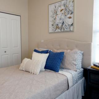 A cozy bedroom with a neatly made bed, featuring blue and white pillows, decorated with floral artwork on the wall.