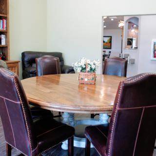 A conference room with a round wooden table and leather chairs, accompanied by a bookcase.