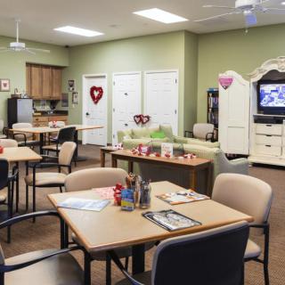 A cozy community room with tables and chairs, a kitchenette, festive decorations, and a television.