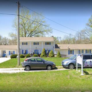 A suburban house with a driveway and parked cars, surrounded by a green lawn and trees.