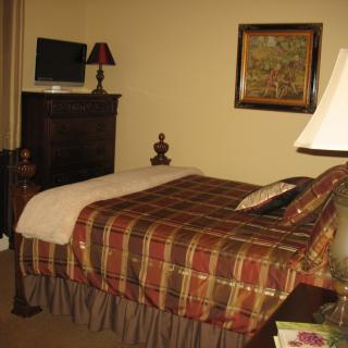 A cozy bedroom with a neatly made bed, television atop a dresser, and warm lighting.