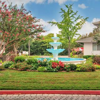 A beautifully landscaped garden featuring a multi-tiered fountain surrounded by colorful flowers and lush greenery.