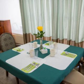 A neatly arranged table with a green and white tablecloth, featuring a flower vase centerpiece, surrounded by chairs and set for four.