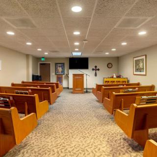 An interior view of a chapel with wooden benches and an altar at the front.