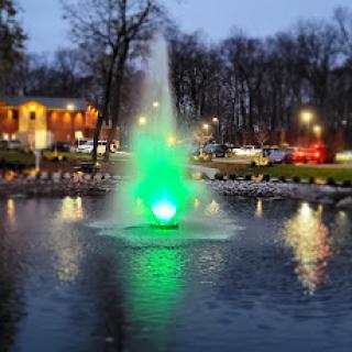 A vibrant green fountain lights up the evening in a serene park setting.