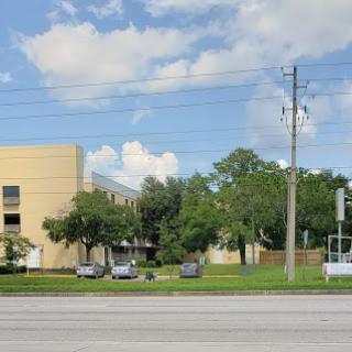 A view of a modern building surrounded by greenery and power lines under a partly cloudy sky.