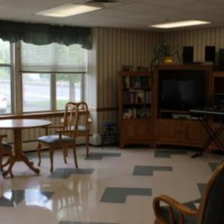 A cozy living room with a television, chairs, and a table near large windows.