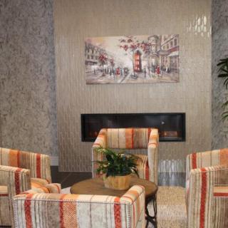 A cozy living room featuring patterned chairs around a small table, with a fireplace and artwork on the wall.