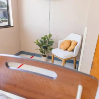A cozy hospital room with a bed, a chair with pillows, and a potted plant by the window.