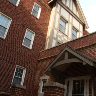 An exterior view of a brick residential building with multiple windows and a gabled entrance.