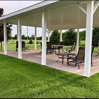 A covered pavilion with patio furniture set on a lush green lawn.