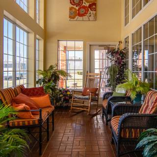 A cozy sunroom filled with natural light, featuring comfortable seating and lush indoor plants.