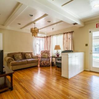 A cozy living room with hardwood flooring, featuring a sofa, armchair, lamp, and chandelier.