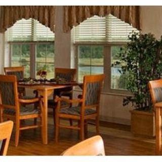 A cozy dining area with a wooden table and chairs near large windows with blinds and curtains.