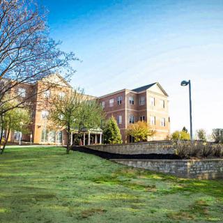A scenic view of a brick building surrounded by green grass and trees under a clear blue sky.