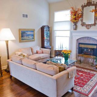 A cozy and well-decorated living room featuring a sofa set, coffee table with flowers, a fireplace adorned with a mirror and floral arrangement, and an elegant rug.
