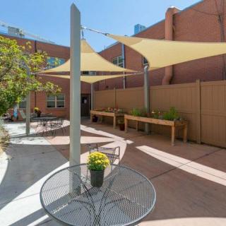 A modern outdoor patio with shade sails, tables, chairs, and potted plants.