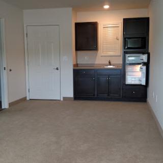A small, empty living space featuring a kitchenette with dark cabinets.