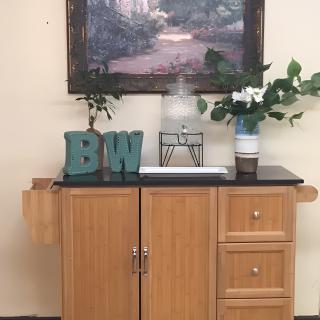 A wooden cabinet with decorative items, including a painting, plants, and letters 'B' and 'W'.