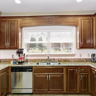 A spacious kitchen with wooden cabinetry, featuring a sink beneath a large window and modern appliances on the countertop.
