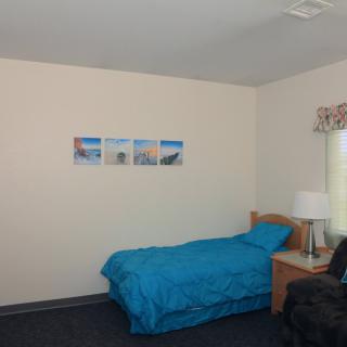 A simple bedroom with a single bed and blue bedding, featuring a nightstand and wall art.