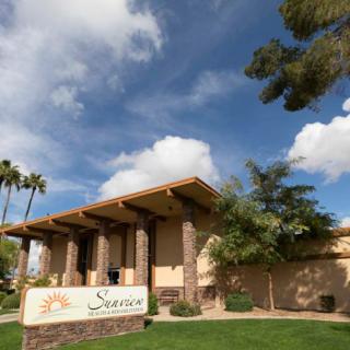 A sunny day view of a building with a sign, surrounded by trees and under a partly cloudy sky.