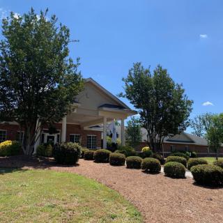 A building surrounded by well-maintained landscaping, including trees and neatly trimmed bushes under a clear blue sky.