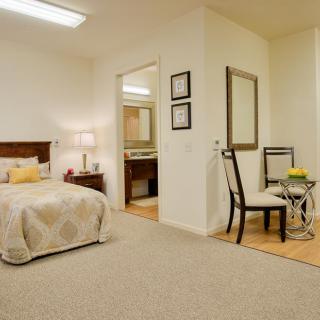 A cozy bedroom with a neatly made bed, desk, and chair, featuring warm lighting and elegant decor.