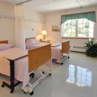 A clean hospital room with two empty beds, large windows, and bright lighting.