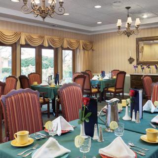An elegantly decorated dining room with neatly arranged tables and chairs, featuring chandeliers and large windows.