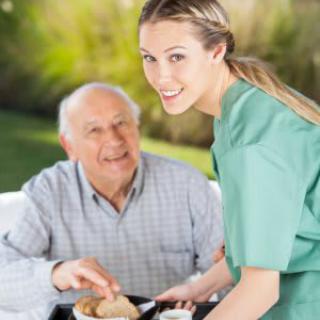 A caregiver assists an elderly man with his meal outdoors.