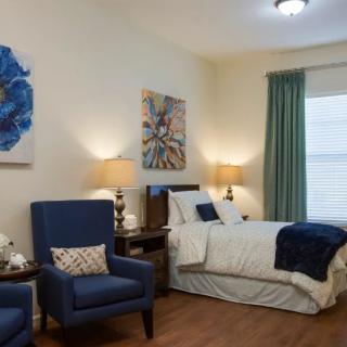A cozy bedroom with a neatly made bed, two armchairs, and decorative artwork on the walls.