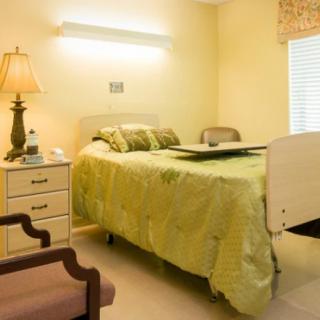 A hospital room with a neatly made bed, nightstand, and a lamp.