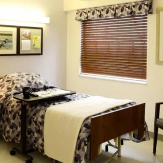 A hospital room featuring a bed, window with blinds, and framed pictures on the wall.