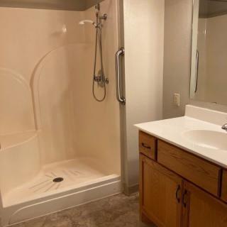A modern bathroom with a shower, sink, and wooden cabinet.
